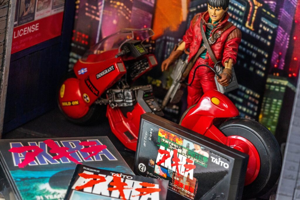 McFarlane Kaneda figure and red motorcycle in a homemade city diorama, with the Akira Famicom cartridge and packaging in front.