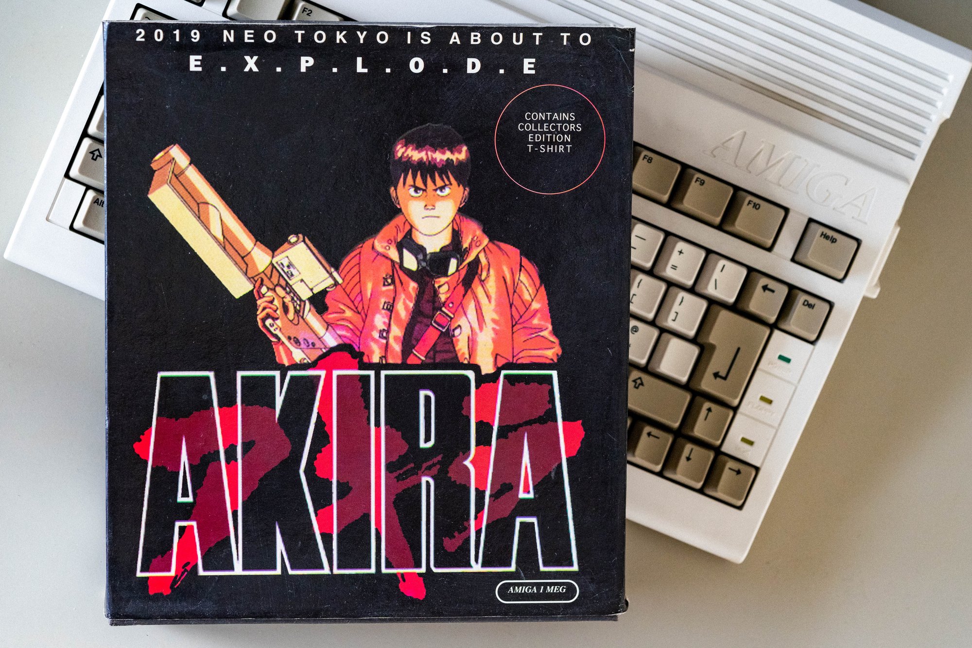 Akira game box resting on an Amiga keyboard, with Kaneda on the cover and a printed collector's T-shirt offer.