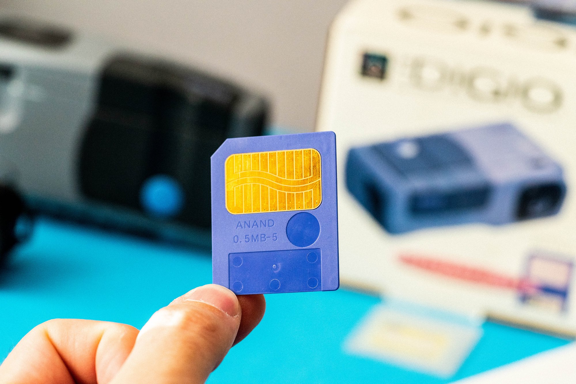 Blue memory card from the Sega Digio, labelled ANAND 0.5MB-5, held in front of the camera and its box.